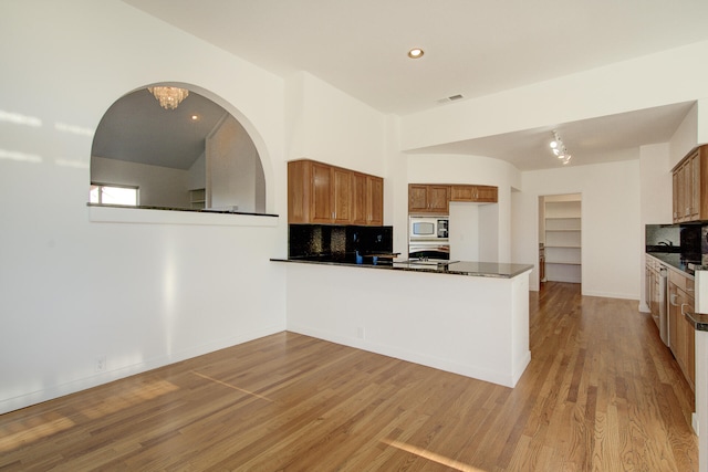 kitchen with backsplash, kitchen peninsula, white microwave, and light hardwood / wood-style floors