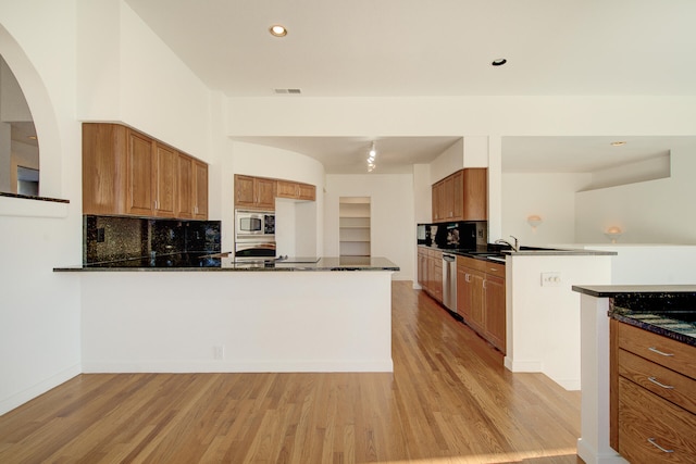 kitchen featuring kitchen peninsula, backsplash, stainless steel appliances, dark stone countertops, and light hardwood / wood-style floors