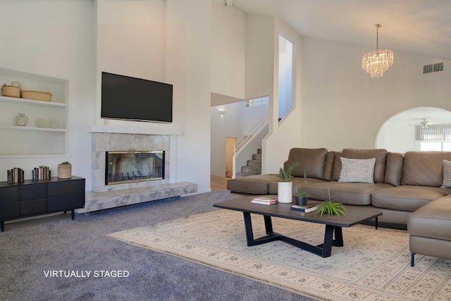 living room featuring a tiled fireplace, light carpet, high vaulted ceiling, and ceiling fan with notable chandelier