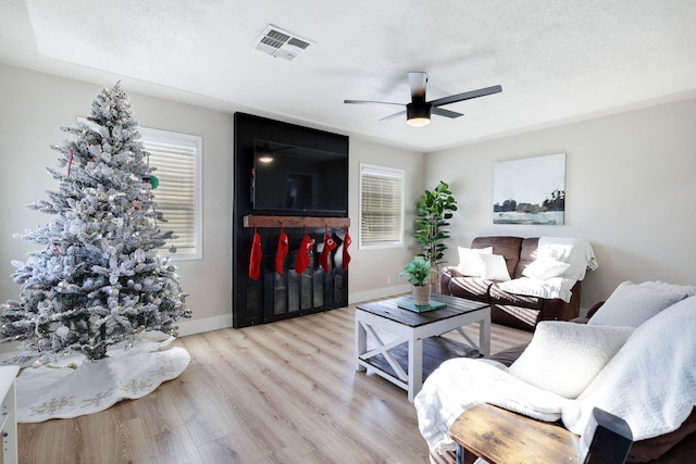 living room featuring a textured ceiling, light hardwood / wood-style floors, ceiling fan, and a healthy amount of sunlight