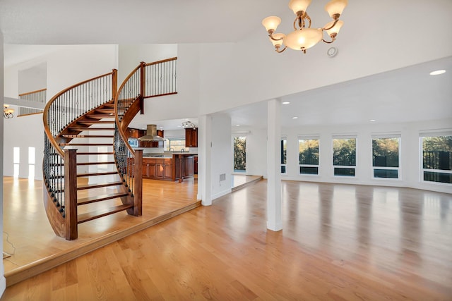 foyer entrance featuring a towering ceiling, light wood-type flooring, and an inviting chandelier