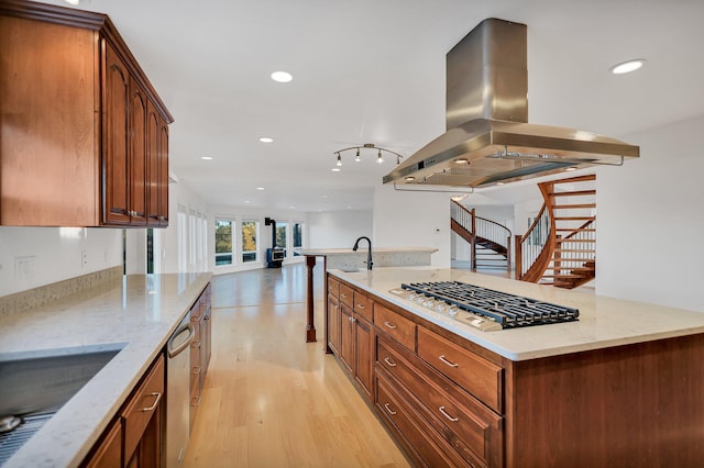 kitchen featuring sink, light stone counters, island exhaust hood, light wood-type flooring, and appliances with stainless steel finishes