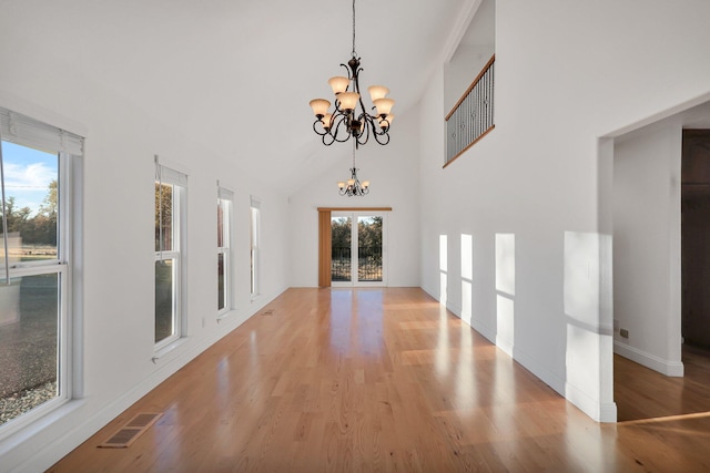 unfurnished living room featuring a chandelier, light hardwood / wood-style flooring, high vaulted ceiling, and a wealth of natural light