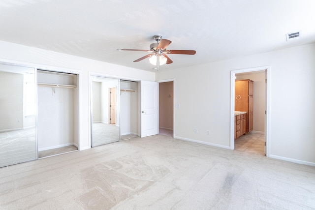 unfurnished bedroom with ensuite bathroom, ceiling fan, light colored carpet, and two closets