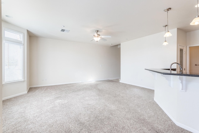 unfurnished living room featuring ceiling fan, sink, carpet, and a healthy amount of sunlight