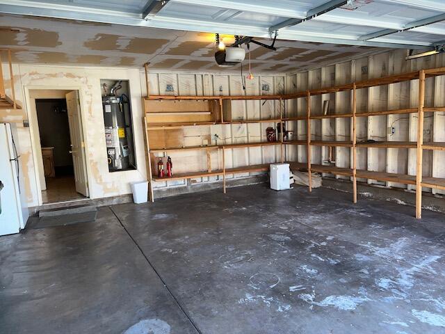 garage featuring a garage door opener, gas water heater, and white refrigerator