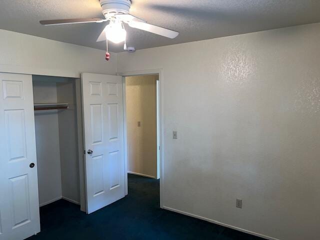 unfurnished bedroom featuring ceiling fan, a textured ceiling, dark carpet, and a closet