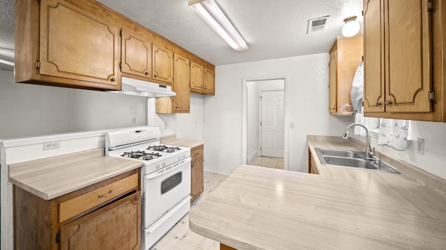 kitchen featuring a sink, light countertops, white gas stove, under cabinet range hood, and visible vents