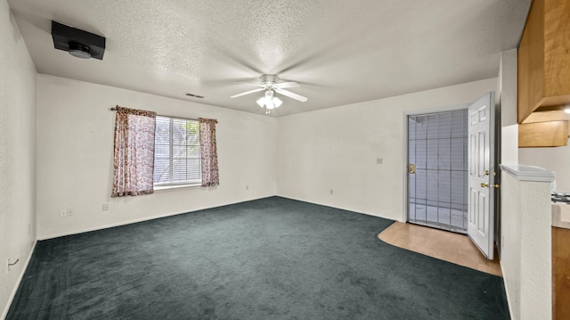 unfurnished room featuring ceiling fan, dark colored carpet, a textured ceiling, and visible vents