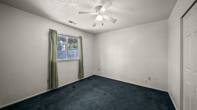 spare room featuring dark colored carpet, a textured ceiling, ceiling fan, and visible vents