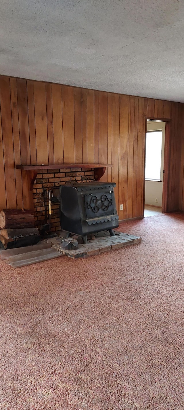 unfurnished living room featuring wood walls, a textured ceiling, and light carpet