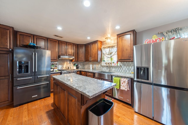 kitchen with high quality appliances, sink, a kitchen island, and light wood-type flooring