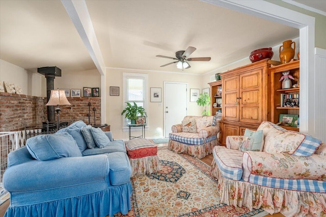 living room with a wood stove, ceiling fan, brick wall, hardwood / wood-style flooring, and ornamental molding