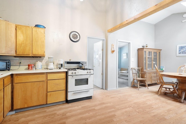 kitchen featuring beam ceiling, gas range gas stove, high vaulted ceiling, light hardwood / wood-style floors, and decorative backsplash