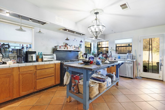 kitchen featuring stainless steel dishwasher, gas range, tile countertops, hanging light fixtures, and light tile patterned flooring