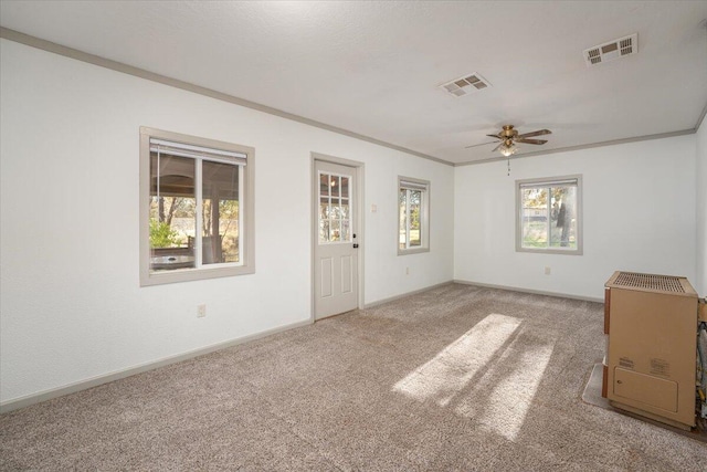 carpeted spare room with ceiling fan, a healthy amount of sunlight, and ornamental molding