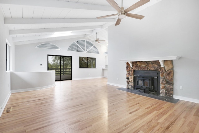 unfurnished living room featuring high vaulted ceiling, beamed ceiling, a wood stove, ceiling fan, and light wood-type flooring