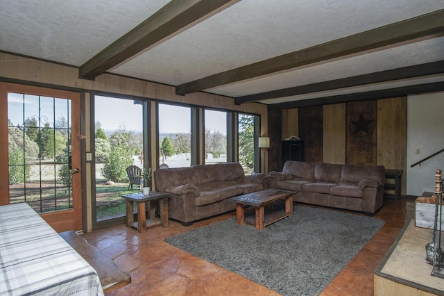 living room featuring beamed ceiling, wood walls, and a textured ceiling