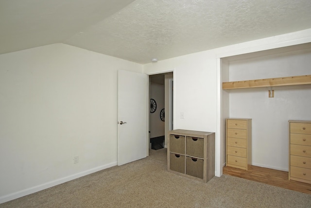 unfurnished bedroom featuring light colored carpet, lofted ceiling, a textured ceiling, and a closet