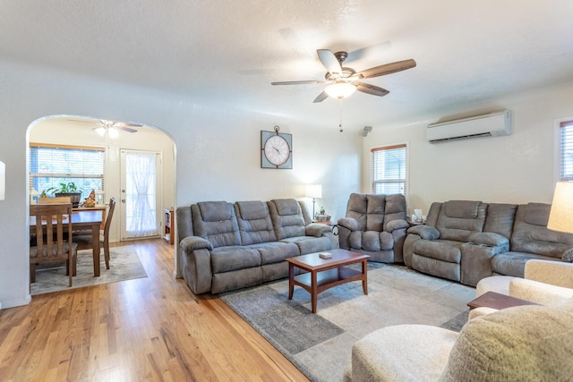 living room featuring ceiling fan, light hardwood / wood-style floors, and a wall unit AC