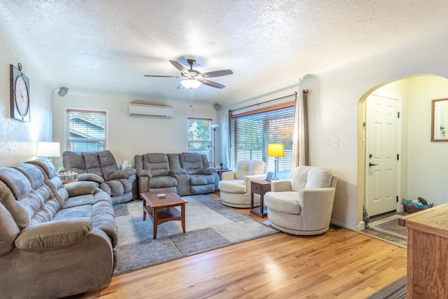 living room with a wall mounted AC, wood-type flooring, a textured ceiling, and a wealth of natural light