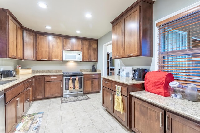 kitchen with light stone countertops, appliances with stainless steel finishes, light tile patterned flooring, and sink