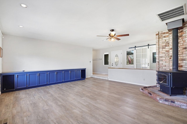 unfurnished living room featuring ceiling fan, a wood stove, and light hardwood / wood-style flooring