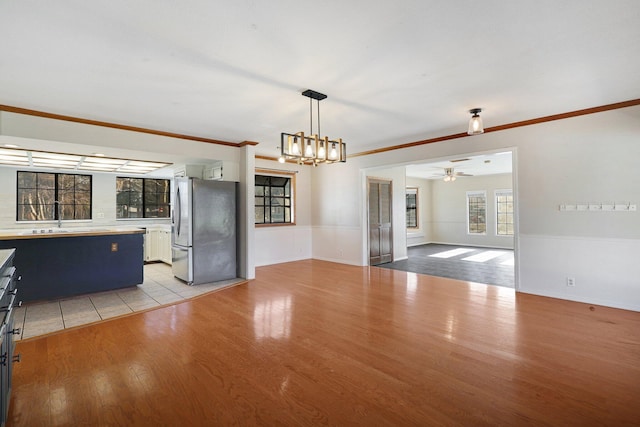 kitchen featuring ornamental molding, ceiling fan with notable chandelier, sink, light hardwood / wood-style floors, and stainless steel refrigerator