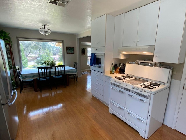 kitchen with light wood-type flooring, a textured ceiling, white cabinets, and white appliances