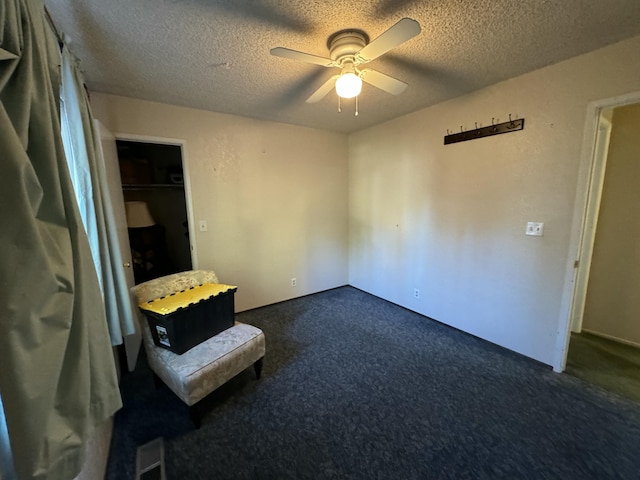 empty room with dark colored carpet, ceiling fan, and a textured ceiling