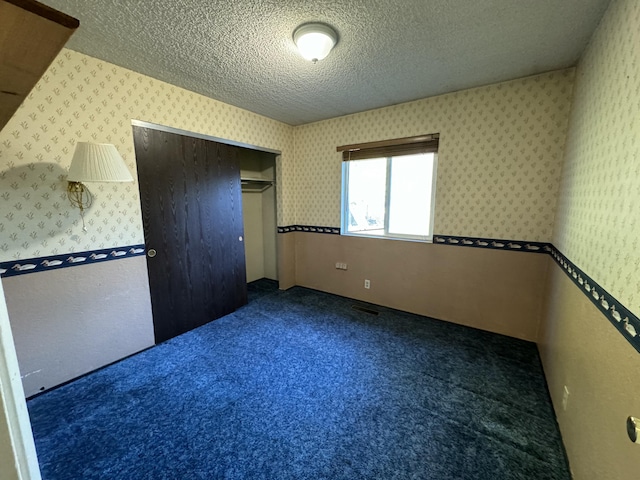 unfurnished bedroom featuring dark carpet, a textured ceiling, and a closet