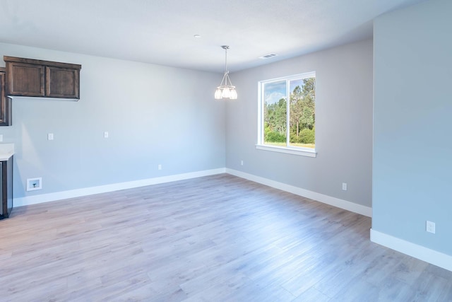 empty room featuring light wood-type flooring and a notable chandelier