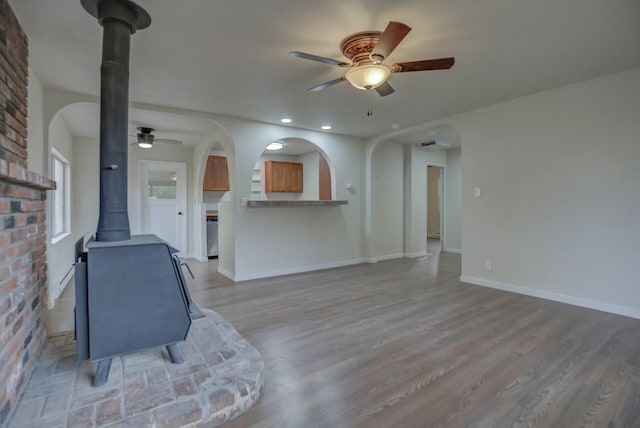 unfurnished living room featuring hardwood / wood-style flooring, a wood stove, ceiling fan, and brick wall