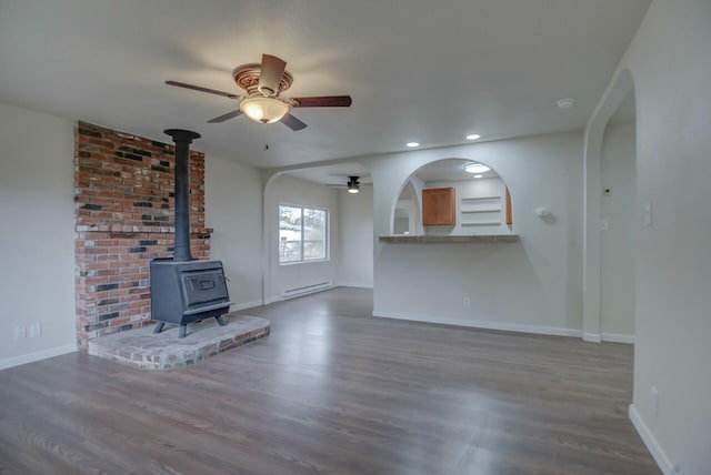 unfurnished living room with a wood stove, ceiling fan, dark hardwood / wood-style flooring, and a baseboard heating unit