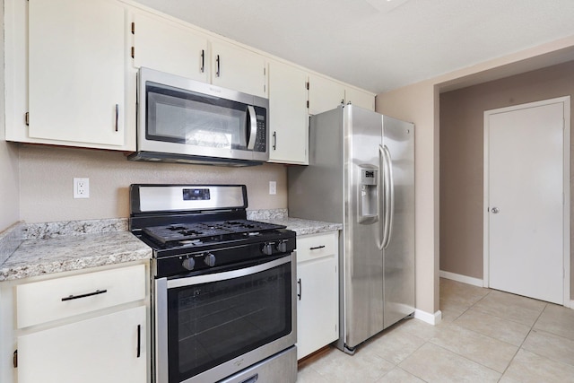 kitchen featuring light stone counters, stainless steel appliances, white cabinetry, and light tile patterned flooring