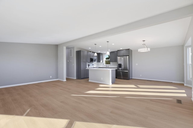 kitchen with sink, a center island, stainless steel appliances, pendant lighting, and light wood-type flooring