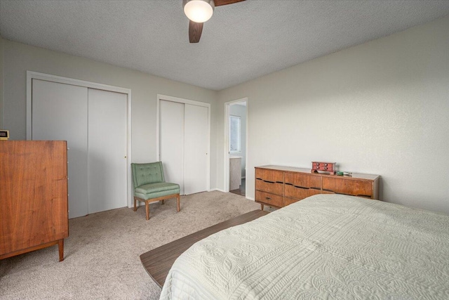 carpeted bedroom with a textured ceiling, ceiling fan, and multiple closets