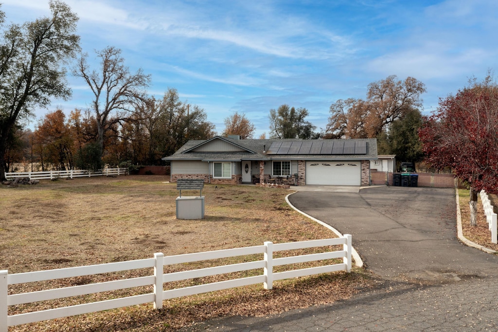 ranch-style home with a front yard, solar panels, and a garage