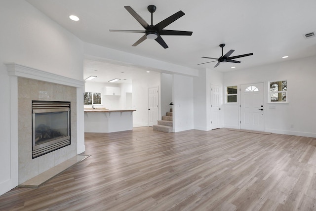 unfurnished living room featuring a tile fireplace, ceiling fan, and light hardwood / wood-style floors