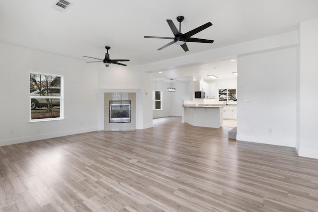 unfurnished living room with light hardwood / wood-style floors, ceiling fan, and a tiled fireplace