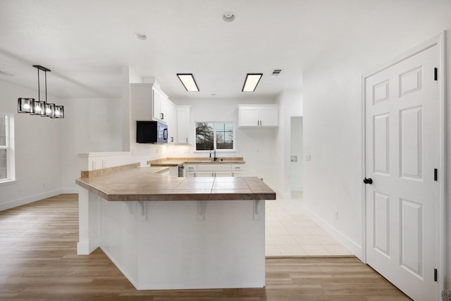 kitchen with kitchen peninsula, a kitchen bar, light wood-type flooring, decorative light fixtures, and white cabinetry