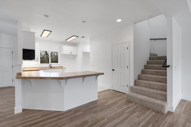 kitchen featuring kitchen peninsula, a kitchen breakfast bar, light wood-type flooring, tile countertops, and white cabinets