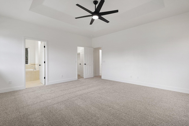 unfurnished bedroom featuring ceiling fan, a raised ceiling, and ensuite bath