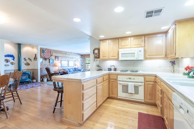 kitchen featuring light brown cabinets, white appliances, kitchen peninsula, and light hardwood / wood-style flooring