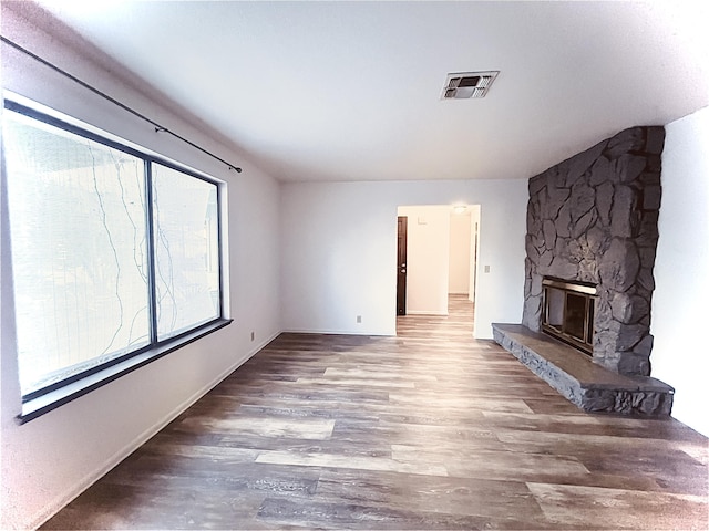 unfurnished living room with a stone fireplace, plenty of natural light, and wood-type flooring