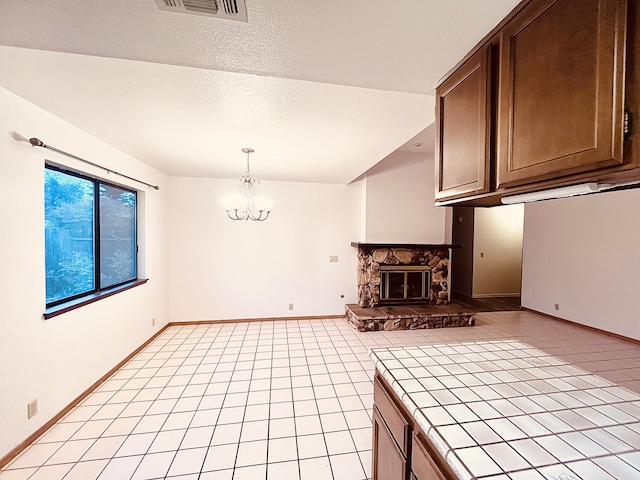 kitchen with tile countertops, a fireplace, a textured ceiling, decorative light fixtures, and a chandelier