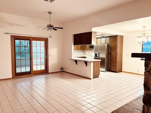 kitchen featuring a breakfast bar, ceiling fan with notable chandelier, decorative backsplash, appliances with stainless steel finishes, and kitchen peninsula