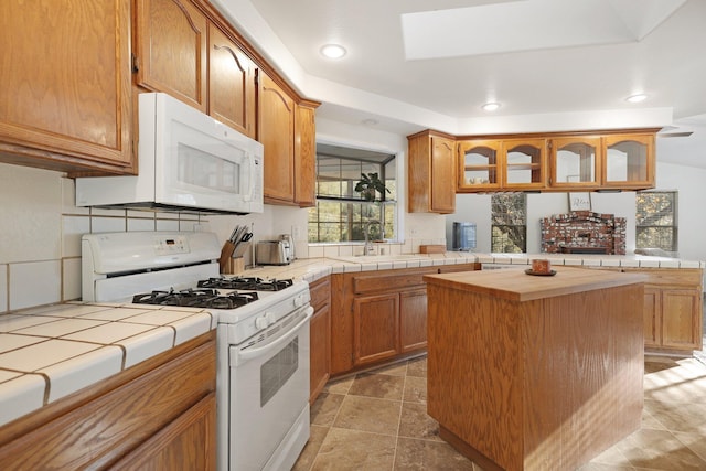 kitchen with a skylight, tile counters, sink, white appliances, and a kitchen island