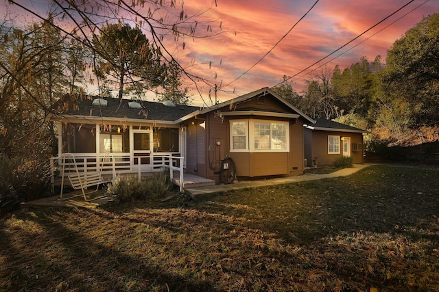 back house at dusk with a sunroom, a deck, and a yard