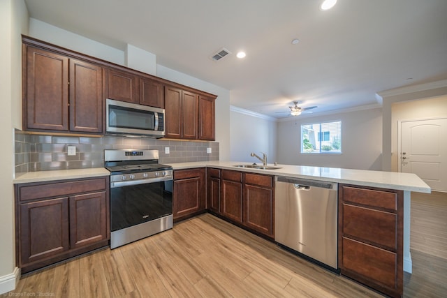 kitchen with light wood-type flooring, kitchen peninsula, sink, and appliances with stainless steel finishes